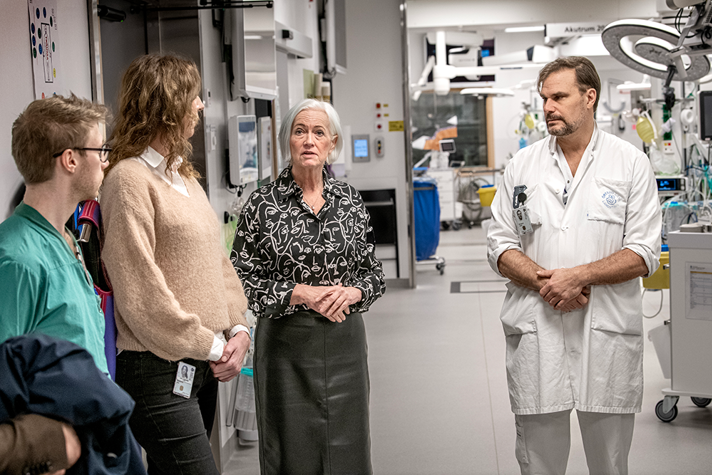 Acko Ankarberg Johansson står i en sjukhuskorridor omgiven av sjukvårdspersonal.