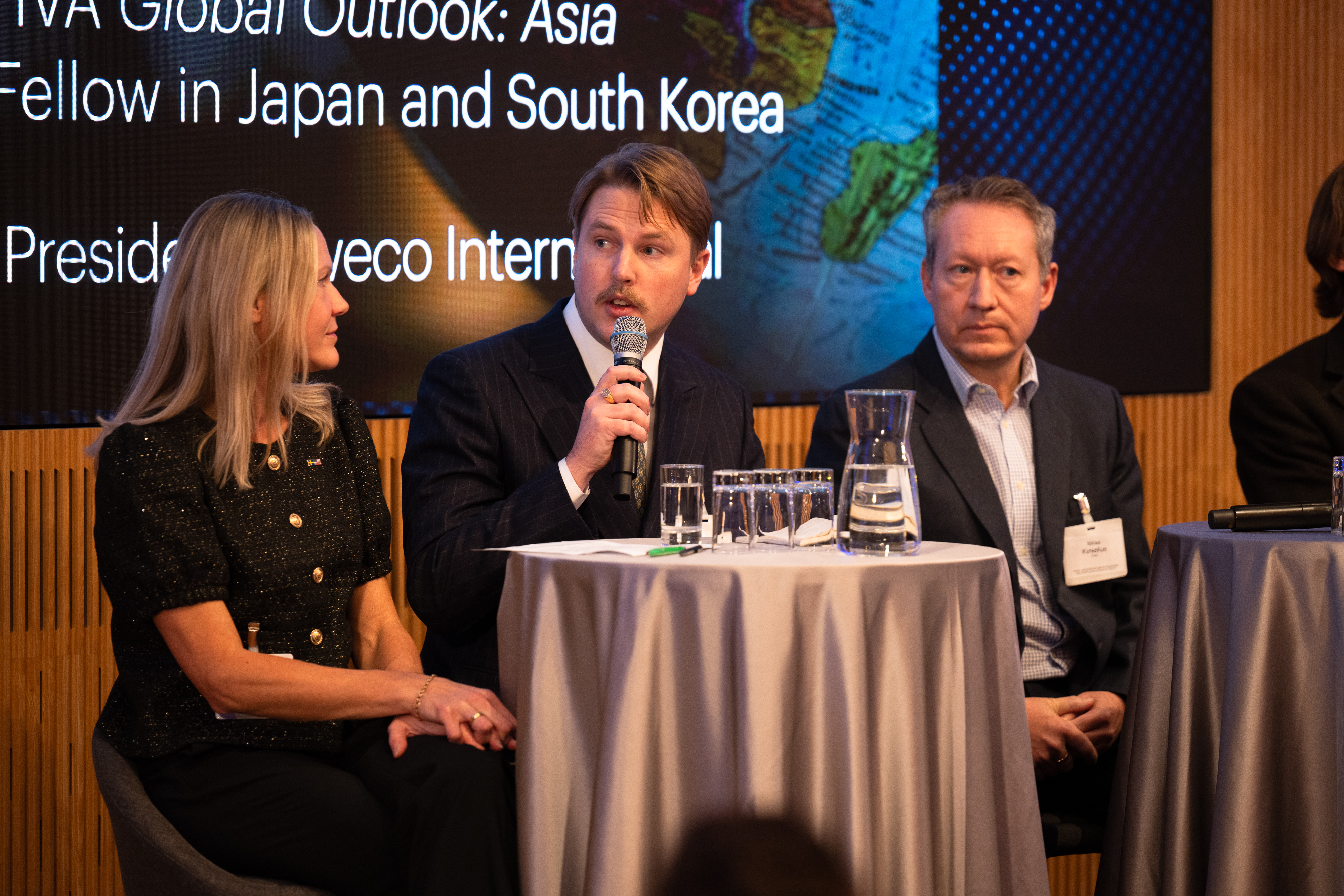 En man talar i en mikrofon, och bredvid honom i soffan sitter en kvinna och en man.