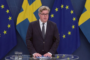 Statsrådet står vid en talarpulpet. Det svenska flaggan i fonden.