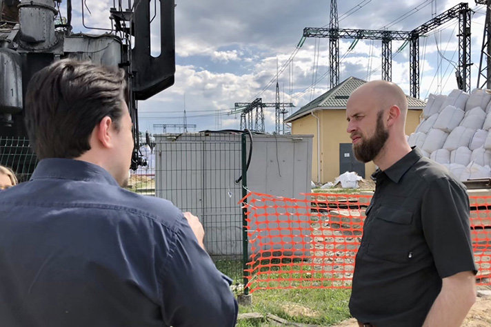 Carl-Oskar Bohlin pratar med en man vid besök på en transformatorstation som är under uppbyggnad efter en rysk attack. 