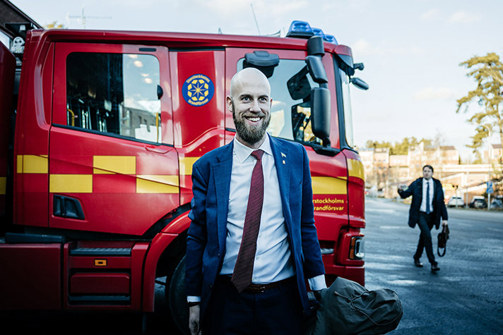 Carl-Oskar Bohlin är glad och står framför ena sidan av en brandbil.  I bakgrunden syns statssekreterare Johan Berggren 