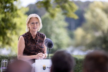 Statsrådet står vid en mikrofon utomhus och talar till medias representanter.