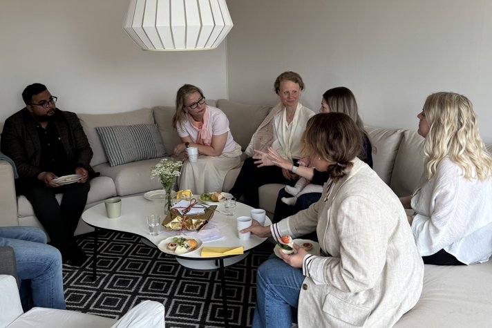 Skolministern och föräldrarna sitter i en soffa i ett vardagsrum och pratar.