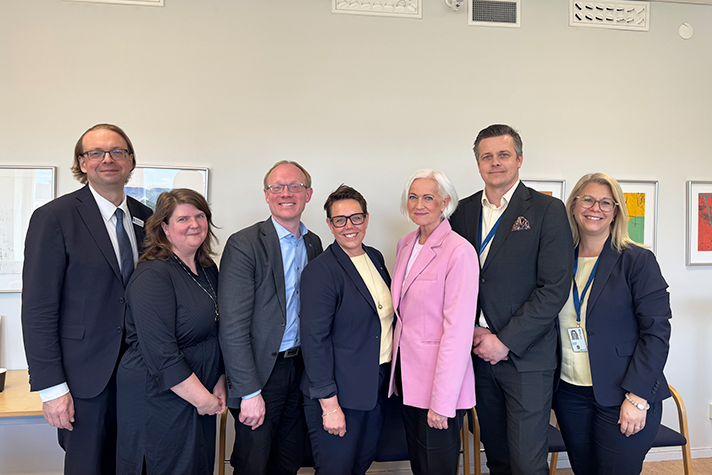 Gruppbild på sju leende personer med ministern i mitten.