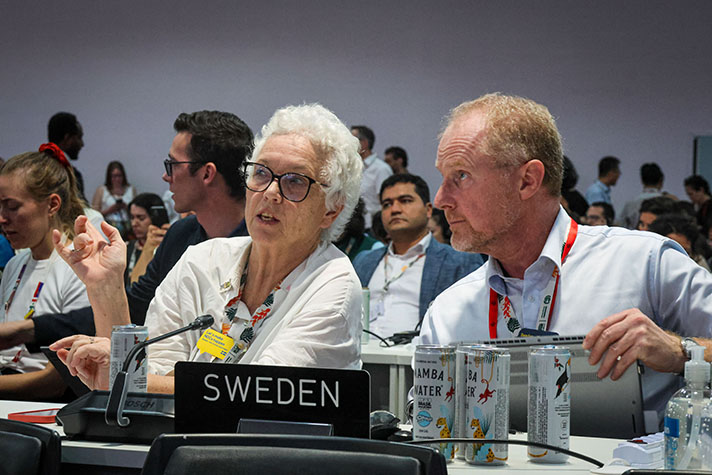 En man och en kvinna siter vid ett bord bakom en skylt med texten Sweden.
