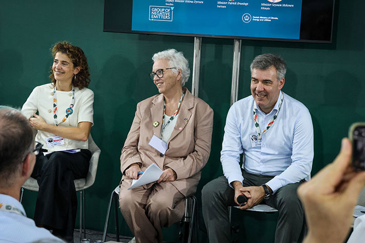 Tre personer sitter bredvid varandra intill en vägg.