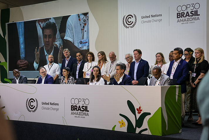 Ett antal människor står bakom ett stort konferensbord med logotyper på framsidan.