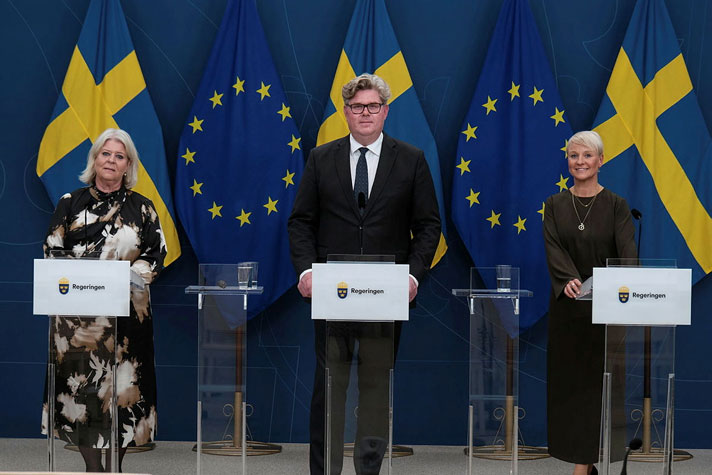 Socialtjänstminister Camilla Waltersson Grönvall, justitieminister Gunnar Strömmer och äldre- och socialförsäkringsminister Anna Tenje står vid var sin talarpulpet. Det är fanor i fonden.