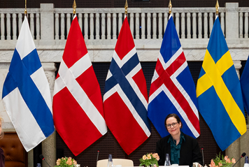 Utrikesministern sitter framför de nordiska flaggorna.