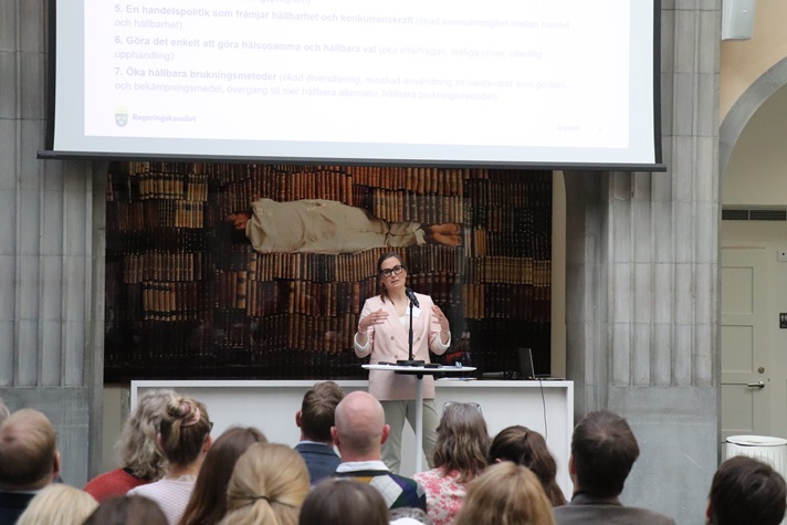 En kvinna i kostym står och pratar framför en publik.