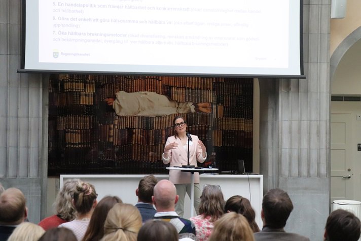 En kvinna i kostym står och pratar framför en publik.