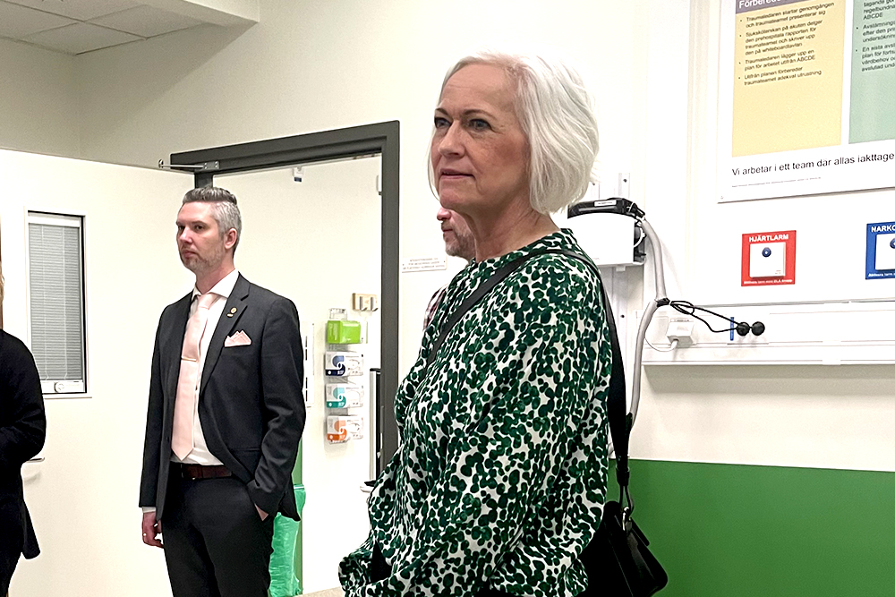 Foto på Acko Ankarberg Johansson på besök på sjukhus. En man i kostym står i bakgrunden.