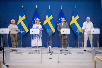 Fyra personer står på podiet vid en pressträff. I bakgrunden EU-flaggor och svenska flaggor.