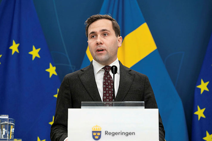 Statsrådet avbildad i halvfigur bakom en talarpupet. Flaggor i fonden.