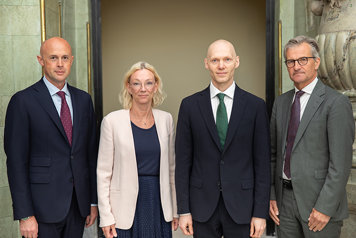 Fyra personer tittar in i kameran, formellt klädda.