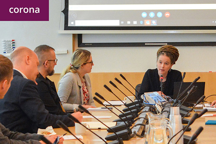 Amanda Lind sitter vid ett bord i ett konferensrum och talar med deltagarna på mötet.