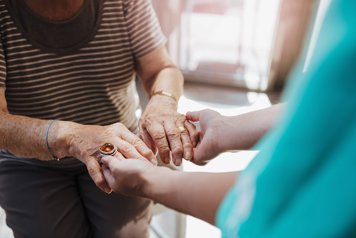 En äldre person håller en vårdgivares händer.