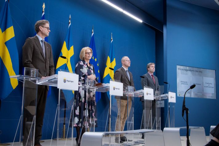 Finansminister Elisabeth Svantesson, Ludvig Aspling, migrationspolitisk talesperson (SD), Hans Eklind, ekonomisk-politisk talesperson (KD) och Jakob Olofsgård, socialförsäkringspolitisk talesperson (L) står vid talarstolar under pressträffen och talar.