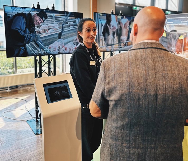 Landsbygdsminister Peter Kullgren står med ryggen mot kameran. Framför honom står en kvinna som pratar. I bakgrunden visas två bildskärmar.