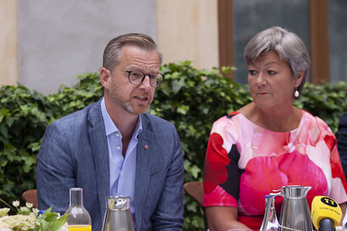 Mikael Damberg och arbetsmarknadsminister Ylva Johansson sitter vid ett bord på en gård. Damberg pratar.