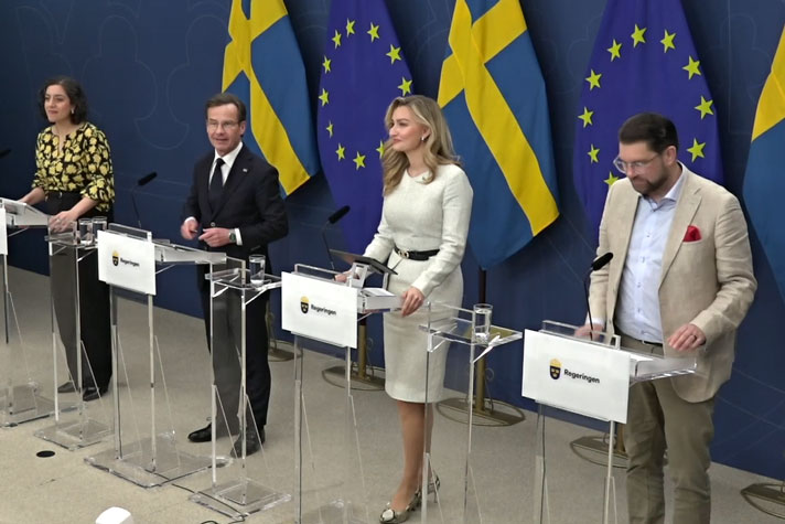 De medverkande står bakom var sin talarstol fotograferade i helfigur snett framifrån.