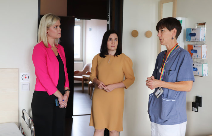 Jämställdhets- och arbetslivsminister Paulina Brandberg och Finlands minister för social trygghet Sanni Grahn-Laasonen står i ett rum tillsammans med en vårdpersonal och samtalar,