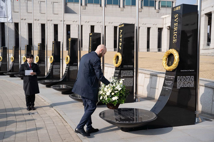 Carl-Oskar lägger ner en krans vid en sten som det står ”Sverige” på.