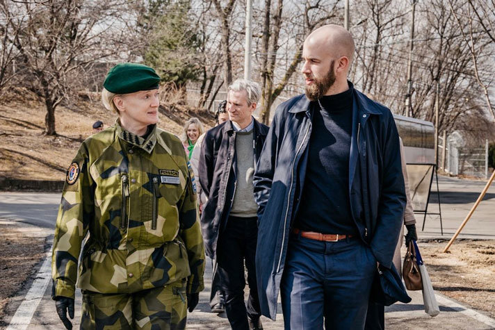 Carl-Oskar gående utomhus i solen med en kvinna i uniform.