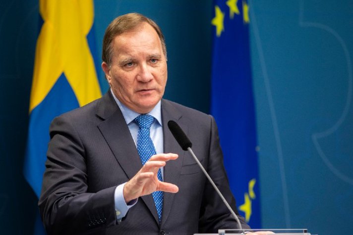 Statsminister Stefan Löfven på en presskonferens vid en mikrofon och blå bakgrund.
