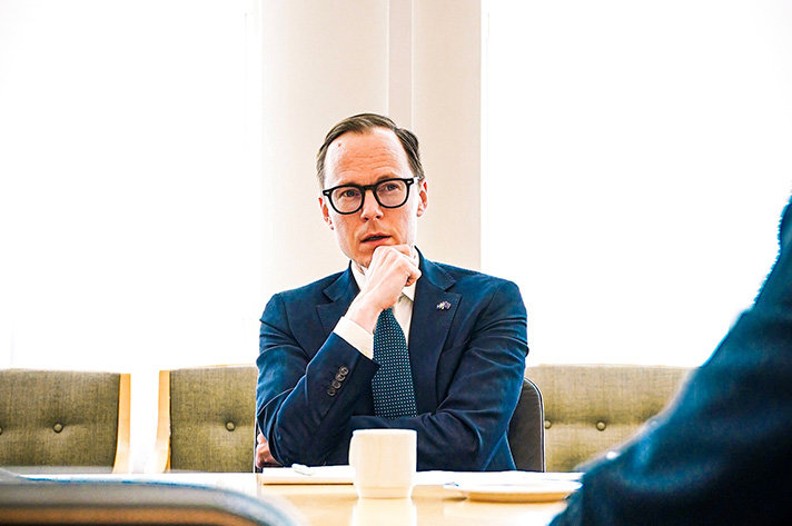 Arbetsmarknads- och integrationsminister Mats Persson sitter vid ett bord i en möteslokal. I förgrunden syns ärmen på personen han talar med.