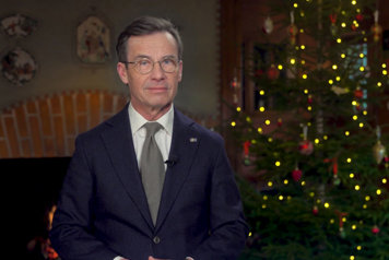 Statsministern är filmad i halvfigur framför en öppen spis samt en julgran i fonden.