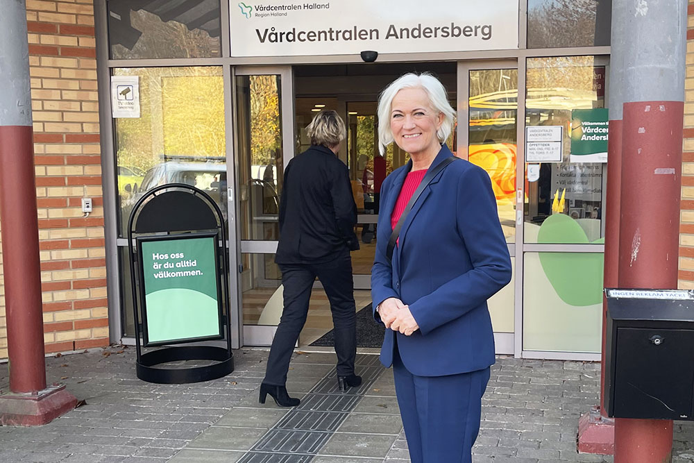 Acko Ankarberg Johansson står framför en entré. Över dörren står det Vårdcentralen Andersberg,