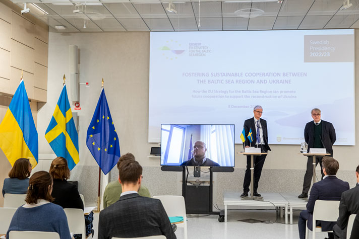 Christian Danielsson och Fredrik Löjdquist står vid varsitt talabord på en scen. Bredvid dem en tv med  Ihor Korkhovyi som är med via länk. I bakgrunden en stor skärm, i förgrunden sittande åhörare och vid sidan av scenen en ukrainsk flagga, en svensk  flagga och EU-flaggan.