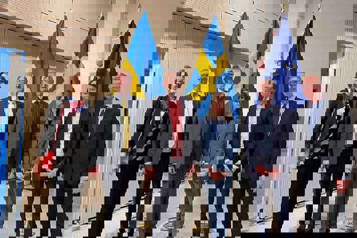 Carolina Bjuggren Glanville, Anders Bergström, Andrij Plachotnjuk, Anna Hagström, Torbjörn Becker, Kurt Bratteby står inomhus bredvid varandra framför en ukrainsk, en svensk och en EU-flagga.