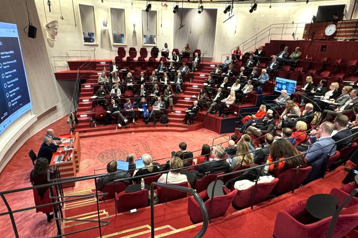 Vi av konferenslokalen med läktare i hästskoform runt ett öppet golv. Alla inredning går i rött.