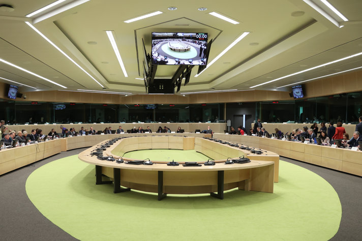 På bilden syns ett stort ovalformat mötesrum, där ministrar sitter vid ett mötesbord längs med väggen. I mitten av rummet står ett bord på en ljusgrön matta.