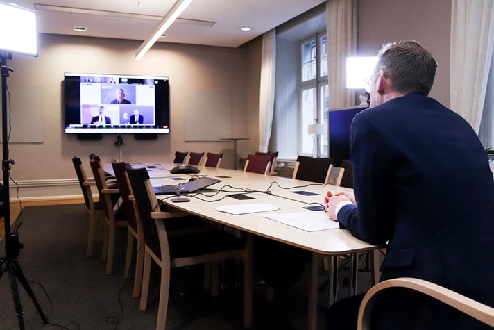 Foto på avlångt konferensrum med en stor skärm, där det pågår en digital konferens.