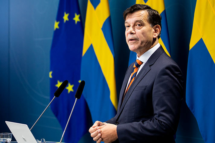 Henrik Landerholm står framför mikrofoner i en presskonferenssal. EU-flaggan och svenska flaggor i bakgrunden.