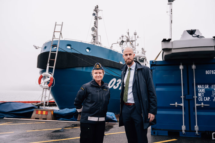 Kustbevakningens generaldirektör Therese Mattsson och minister för civilt försvar carl-Oskar Bohlin står framför ett av Kustbevakningens skepp på en gråmulen dag.