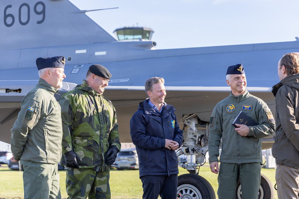 Försvarsminister Pål Jonson skrattar tillsammans med fyra andra personer framför det parkerade planet. 