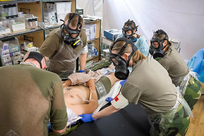 Sjukvårdare med gasmasker runt en man på en bår.