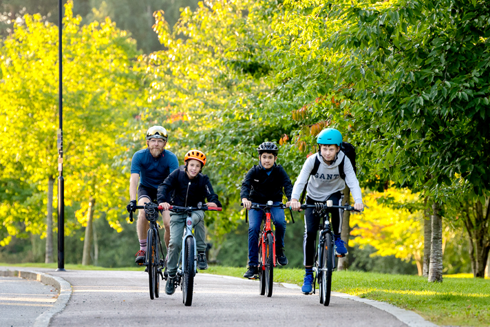 En man och tre barn cyklar i det gröna.