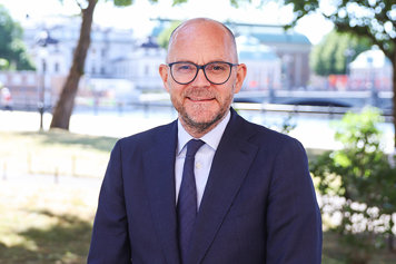 Statsrådet Johan Britz fotad utomhus. Grönska syns i bakgrunden och statsrådet ser glad ut.