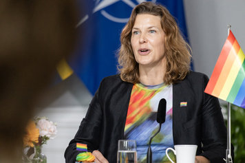 Jämställdhetsminister Nina Larsson sitter ner och talar. Bredvid henne syns en pride-flagga och statsrådet bär en pin med Prideflagga.