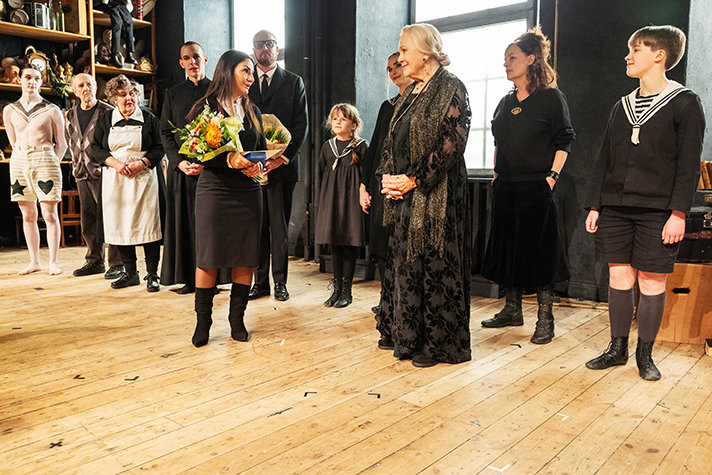 Christina Schollin på scen omgiven av sina medspelare, håller upp medaljen.