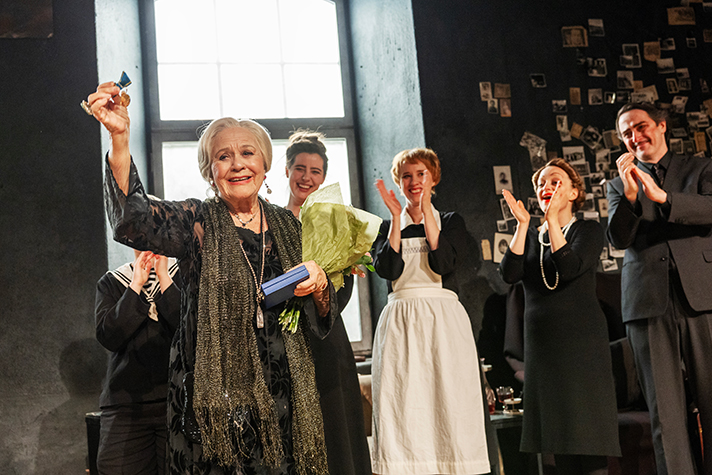 Christina Schollin på scen omgiven av sina medspelare, håller upp medaljen.