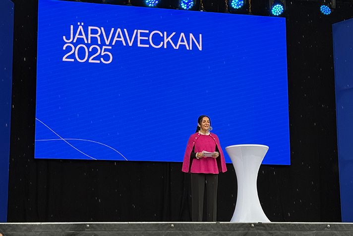 Kulturminister Parisa Liljestrand står på en scen och pratar inför publiken framför en blå bakgrund