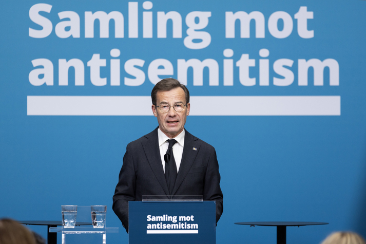 Statsministern vid en talarstol, i bakgrunden texten Samling mot antisemitism