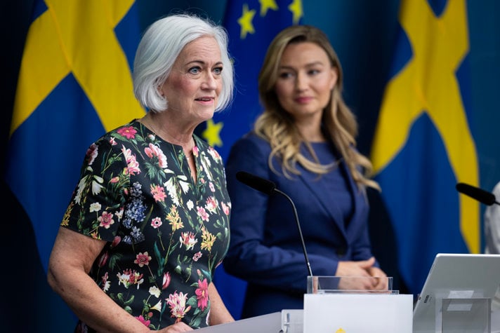 Porträtt av Acko Ankarberg Johansson och Ebba Busch på en presskonferens. Bakom dem finns svenska flaggor och EU-flaggor.