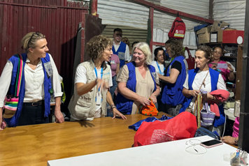 Flera personer står runt ett bord och pratar med varandra. De har på sig blåa västar som kännetecknar organisationen Unicef.